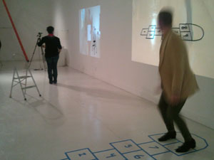 A participant in the 'Becoming Wendy' performance plays hopscotch while looking at a digital projection of the playing field. 
