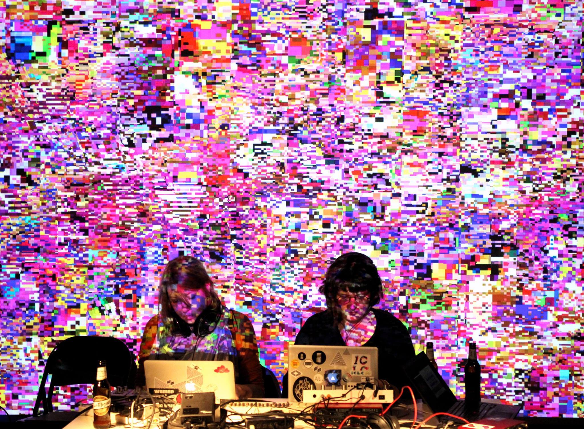 Two women sitting behind computer screens with colorful code displayed behind them
